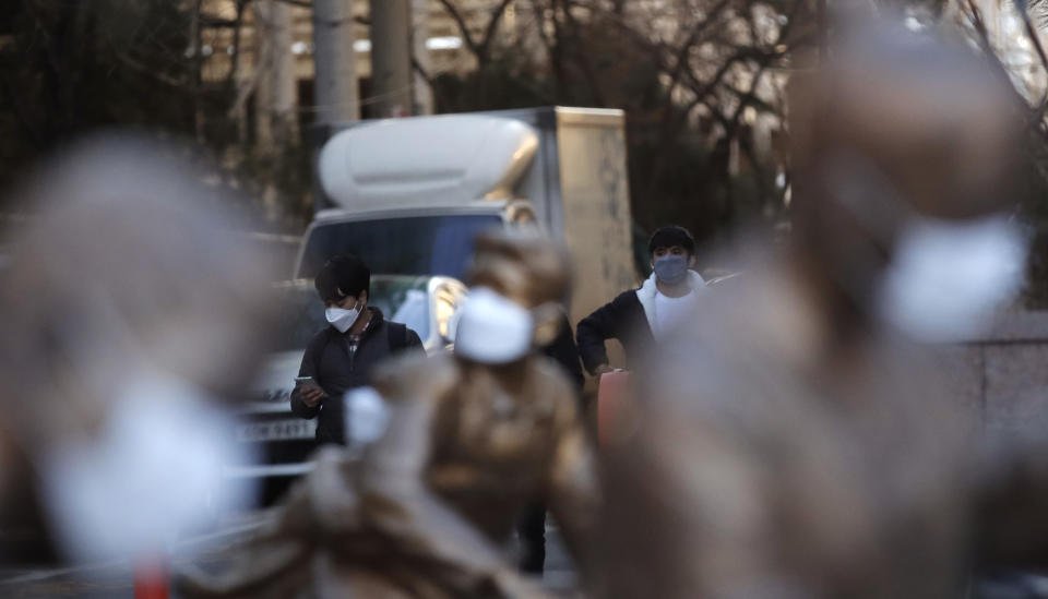 Pedestrians wearing face masks as a precaution against the coronavirus, walk near the statues with masks in Incheon, South Korea, Sunday, Feb. 7, 2021. (AP Photo/Lee Jin-man)