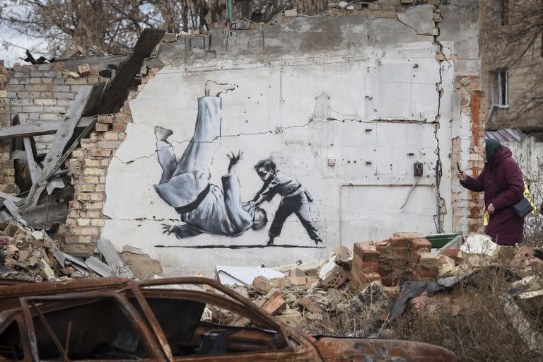 Una mujer toma una fotografía de una obra de arte en un edificio destruido por los combates en Borodyanka, región de Kyiv, Ucrania, el 13 de noviembre de 2022. La obra de arte supuestamente fue realizada por el artista callejero británico Banksy