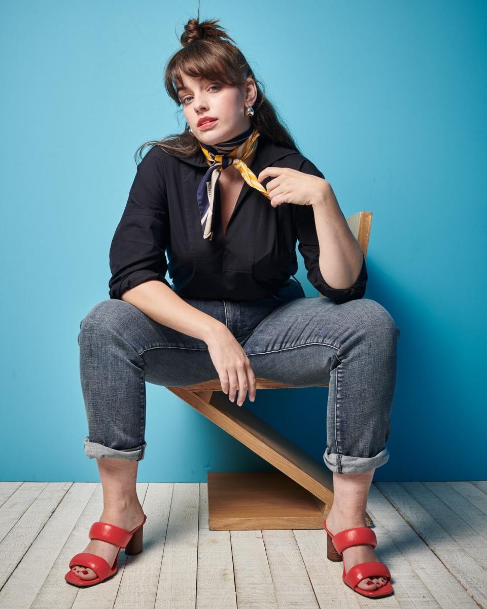 Woman sitting on a chair wearing denim and red sandals with a blue background