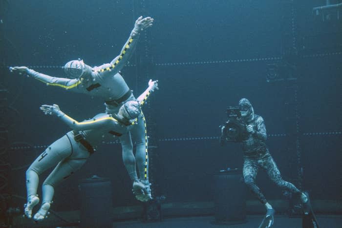 Two actors float in the water while a man films