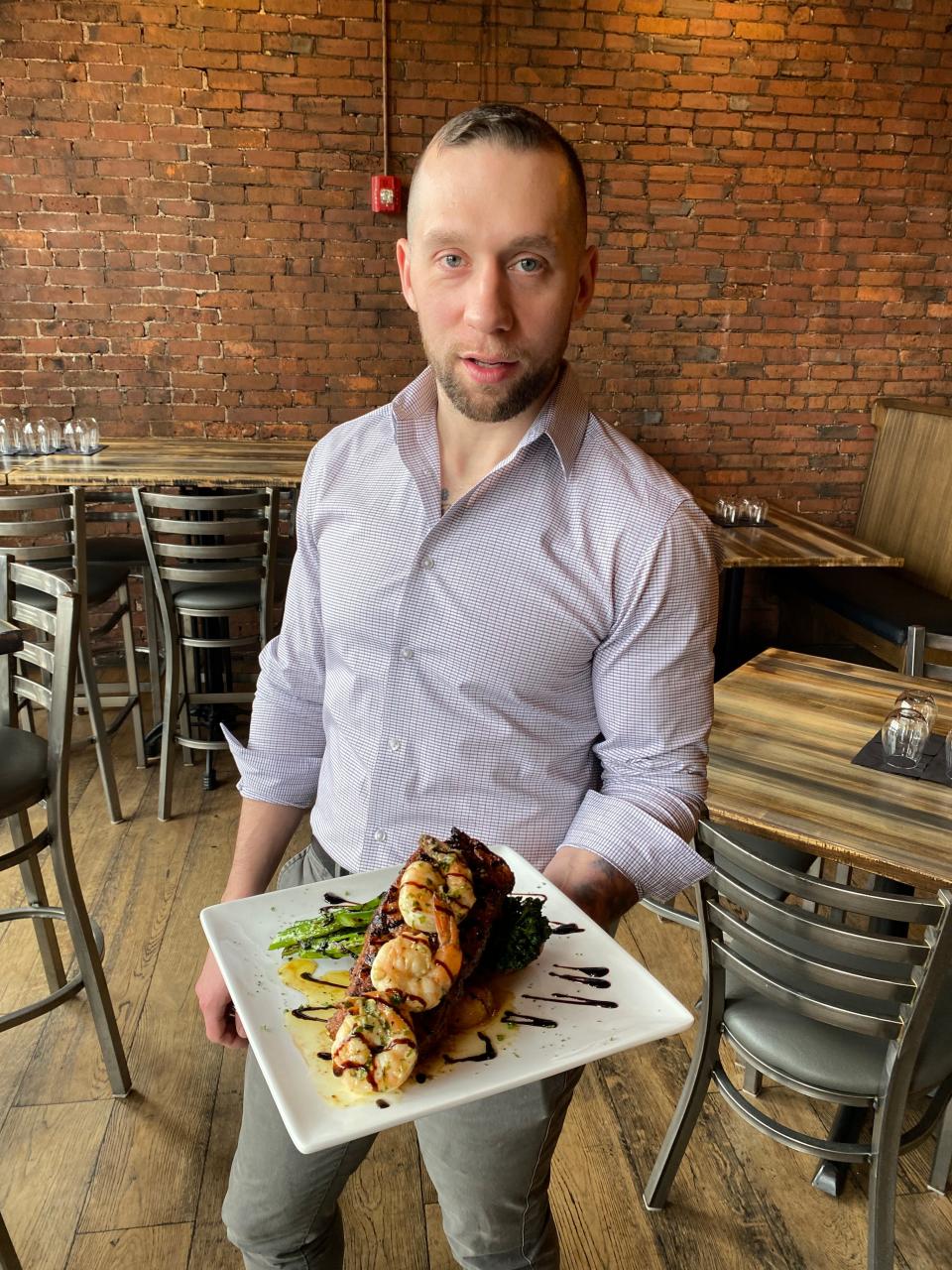 Director of Operations at Union Straw restaurant in Taunton Craig Carreira holds up a plate of the restaurant's sirloin with shrimp, consisting of a 12-ounce grilled sirloin, pee wee potatoes, slow roasted in duck fat, asparagus, herbed garlic butter and a balsamic reduction, on Friday, Jan. 19, 2024.