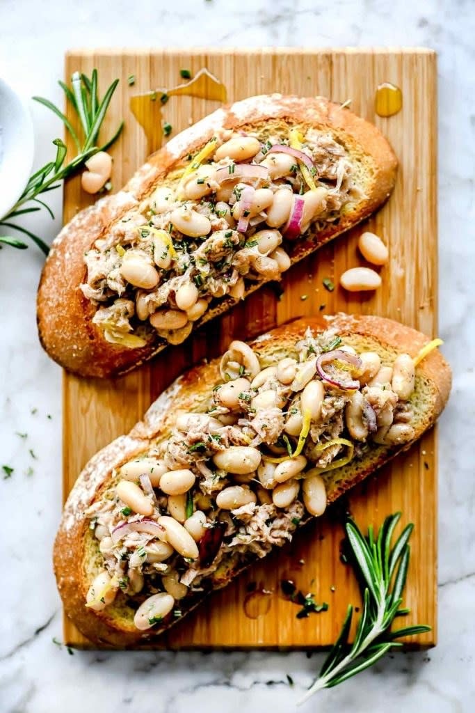 Two slices of toast topped with white beans, tuna, and onion.