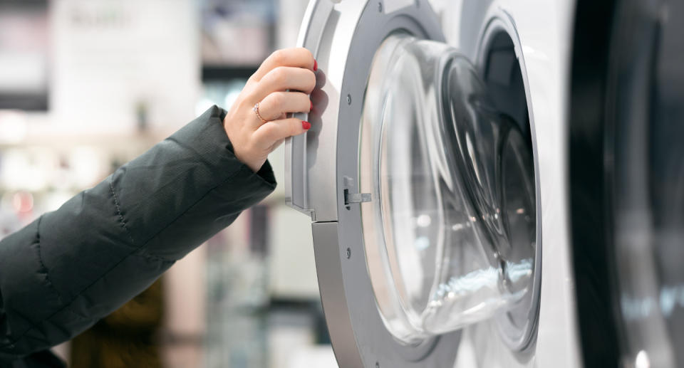 Pictured is a stock image of a hand opening a washing machine.