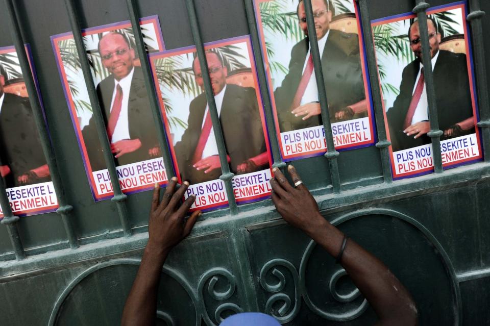 A supporter of former Haitian leader Jean-Bertrand Aristide displays posters of him in 2014. <a href="https://www.gettyimages.com/detail/news-photo/supporter-of-former-haitian-president-jean-bertrand-news-photo/453617532?adppopup=true" rel="nofollow noopener" target="_blank" data-ylk="slk:Hector Retamal/AFP via Getty Images;elm:context_link;itc:0;sec:content-canvas" class="link ">Hector Retamal/AFP via Getty Images</a>