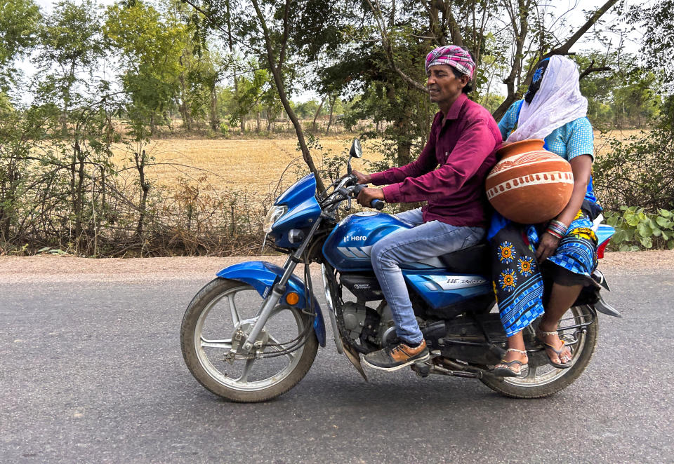 A woman carrying an earthen pot used for storing water pillion rides on a motorcycle on a hot summer afternoon in Lalitpur district in northern Uttar Pradesh state, India, Sunday, June 18, 2023. Swaths of two of India's most populous states are under a grip of sever heat leaving dozens of people dead in several days as authorities issue a warning to residents over 60 and others with ailments to stay indoors during the daytime. (AP Photo/Rajesh Kumar Singh)