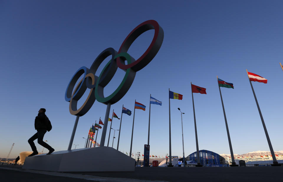 A man poses for a photo beneath the Olympic rings at Olympic Park, prior to the 2014 Winter Olympics, Monday, Feb. 3, 2014, in Sochi, Russia. (AP Photo/Robert F. Bukaty)