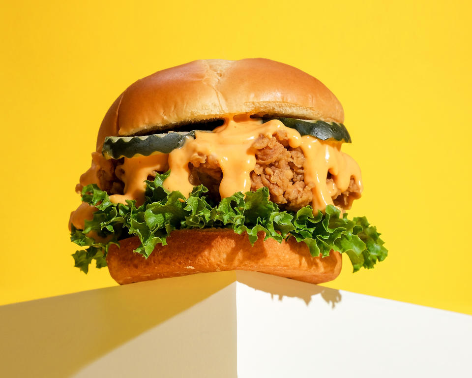 Chicken sandwich with lettuce and sauce on a bun, against a yellow background and resting on a white surface