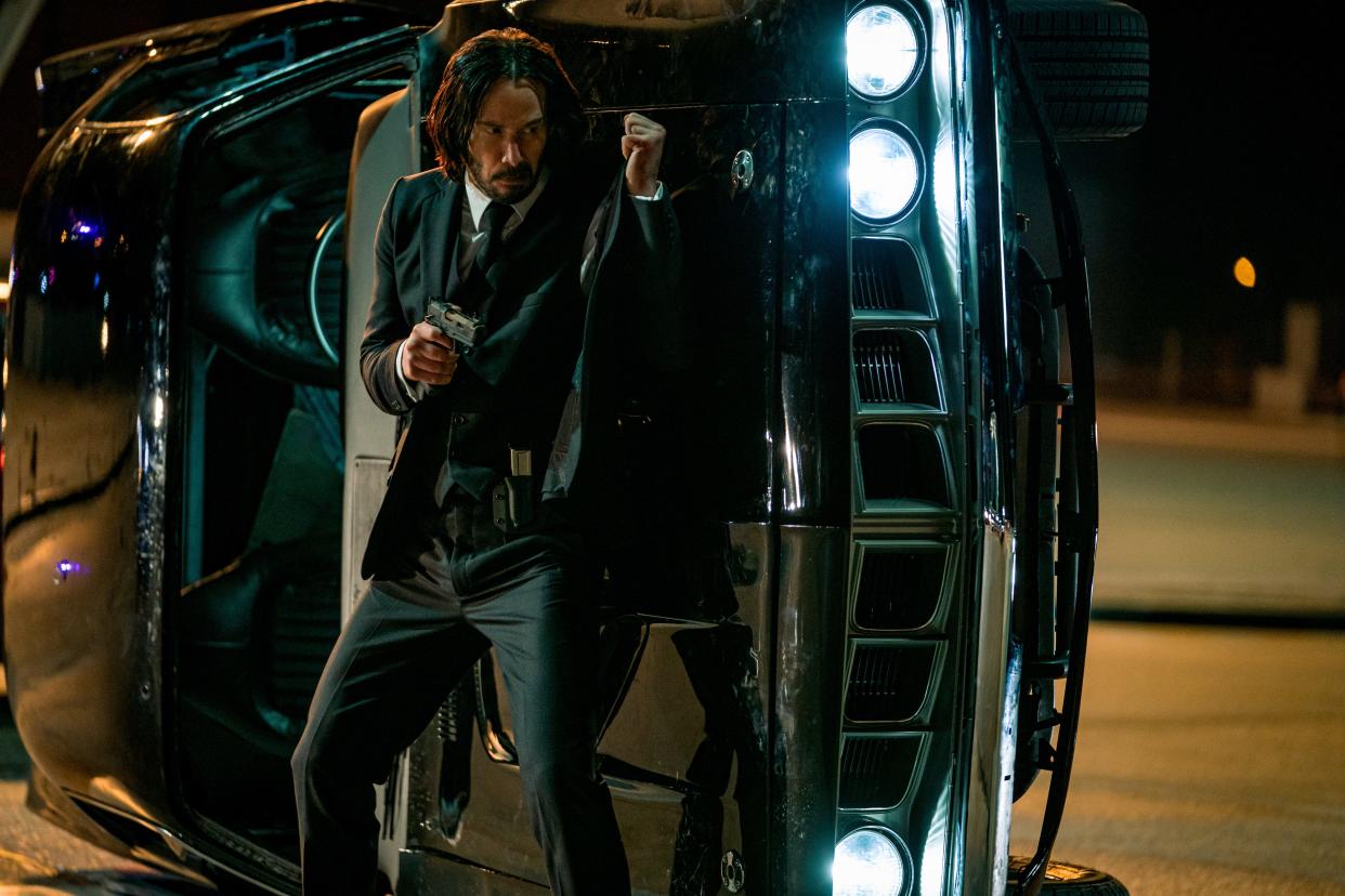 John Wick (Keanu Reeves) uses a car as a shield from well-armed bad guys in the action film "John Wick: Chapter 4."