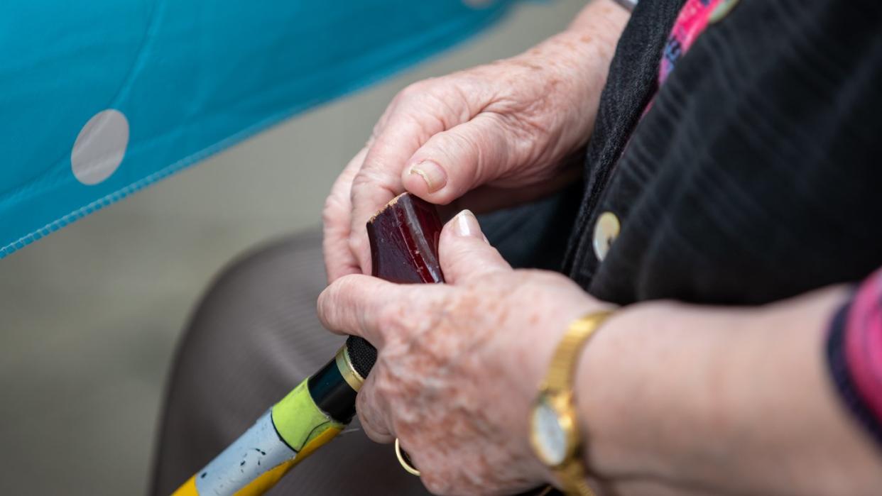 Eine Seniorin sitzt mit ihrem Gehstock im Garten eines Pflegeheims.