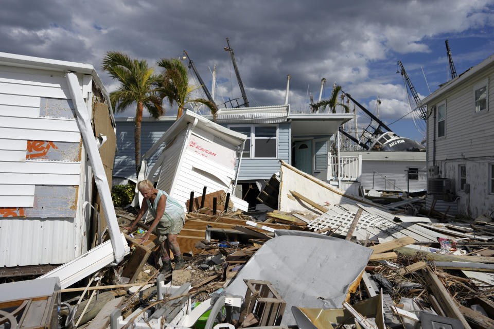 FILE - Kathy Hickey, 70, carefully picks her way through debris from destroyed trailers in the mobile home park where she and her husband Bruce had a winter home on San Carlos Island in Fort Myers Beach, Fla., Oct. 5, 2022, one week after the passage of Hurricane Ian. Costly weather disasters kept raining down on America last year, pounding the nation with 18 climate extremes that caused at least $1 billion in damage each, totaling more than $165 billion, federal climate scientists calculated Tuesday, Jan. 10, 2023. (AP Photo/Rebecca Blackwell, File)