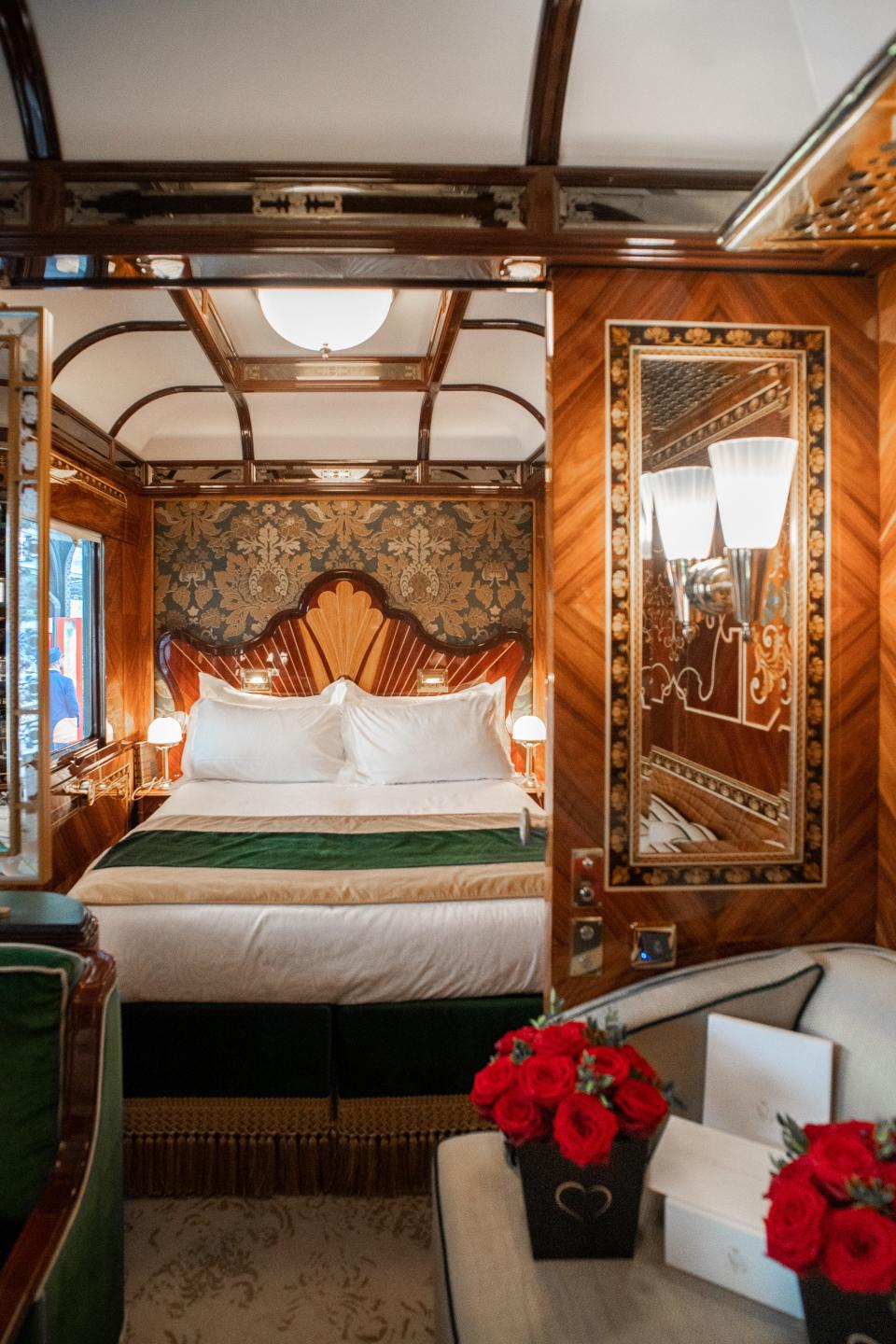 Inside a wood-walled train suite with white and green furnishings, including a seat on the left, a couch on the right, and a bed in the back center.