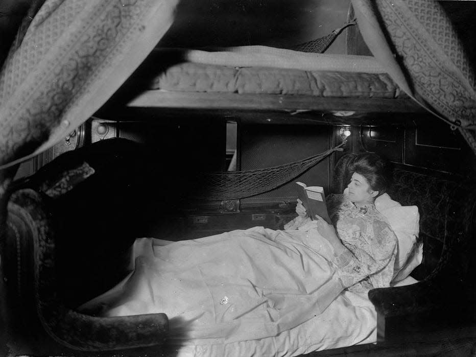 A black and white photo of a woman reading in a sleeper car in 1905.