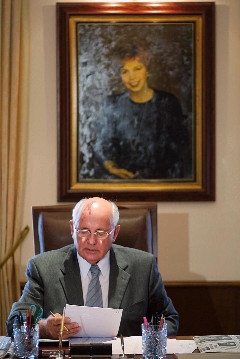 FILE - Former Soviet President Mikhail Gorbachev reads some notes in his office with a portrait of his late wife Raisa in the background, at the Gorbachev Fund in Moscow, Tuesday, Aug. 14, 2001. When Mikhail Gorbachev is buried Saturday at Moscow's Novodevichy Cemetery, he will once again be next to his wife, Raisa, with whom he shared the world stage in a visibly close and loving marriage that was unprecedented for a Soviet leader. Gorbachev's very public devotion to his family broke the stuffy mold of previous Soviet leaders, just as his openness to political reform did. (AP Photo/Alexander Zemlianichenko, File)