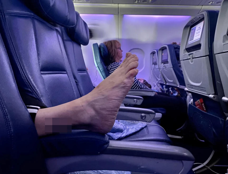 Someone's foot on the arm rest of a plane