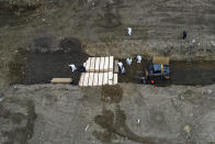 Workers wearing personal protective equipment bury bodies in a trench on Hart Island, Thursday, April 9, 2020, in the Bronx borough of New York. On Thursday, New York City’s medical examiner confirmed that the city has shortened the amount of time it will hold on to remains to 14 days from 30 days before they will be transferred for temporary internment at a City Cemetery. Earlier in the week, Mayor Bill DeBlasio said that officials have explored the possibility of temporary burials on Hart Island, a strip of land in Long Island Sound that has long served as the city’s potter’s field. (AP Photo/John Minchillo)