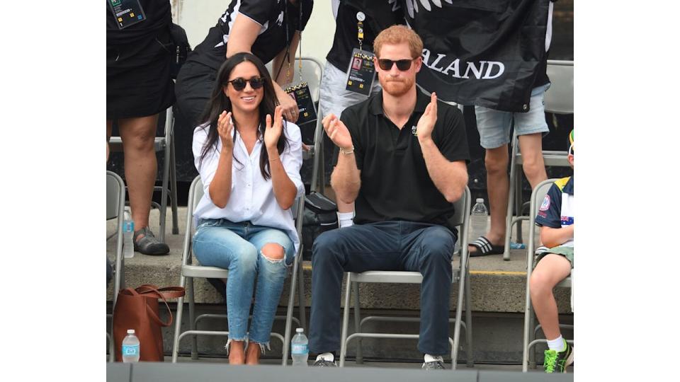 Meghan in super casual ripped jeans sitting with prince harry