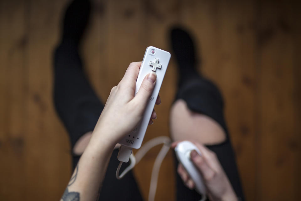 Gothenburg, Sweden - January 17, 2015: A shot from above of a young woman's hands holding Wii remote with Nunchuck, a game pad controller for the Nintendo Wii video game console developed by Nintendo Co., Ltd. Natural lighting. Shot on wooden background.