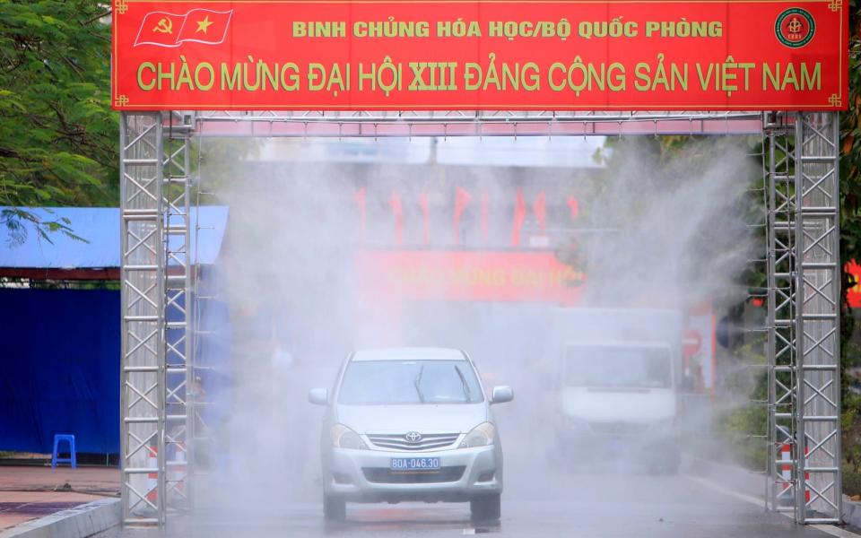 A car is driven through disinfectant mist to enter the venue of Vietnam Communist party congress in Hanoi - AP