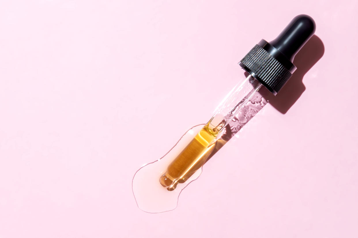 Retinol beauty face oil dripping from dropper with black lid on pink background. Amazon serum, Amazon vitamin c serum, Amazon anti-aging serum