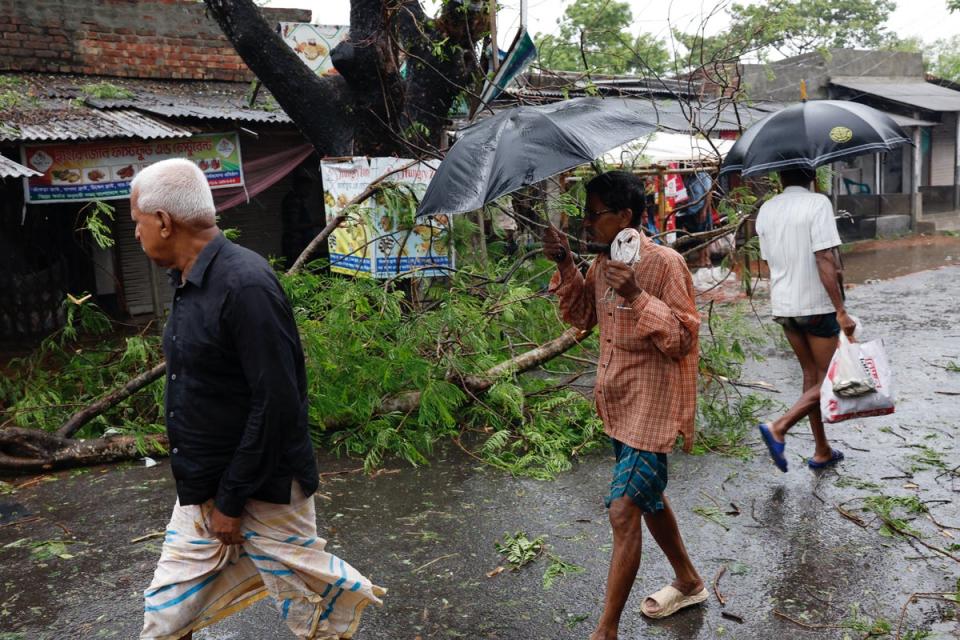 People walk past a fallen tree branch as Cyclone Remal hits the country, in the Shyamnagar area of Satkhira (Reuters)