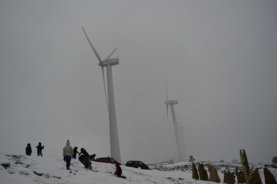 People enjoy the snow near wind turbines in El Perdon mountain, northern Spain, Thursday, Feb. 23, 2023. Spain is building on its reputation in renewable energy to position itself as Europe's future leader in green hydrogen. But some energy sector experts express caution over ramping up an industry that would be wholly reliant on massive increases in the availability of zero-carbon electricity made from sources like wind or solar. (AP Photo/Alvaro Barrientos)