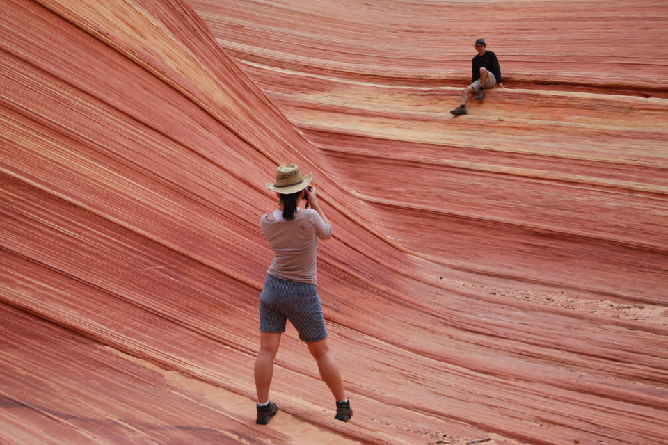 FILE - In this May 28, 2013, file photo, a hiker takes a photo on a rock formation known as The Wave in the Vermilion Cliffs National Monument in Arizona. Outdoor enthusiasts and nature photographers hoping to explore the colorful, contoured landscape of the hugely popular trail in the U.S. Southwest will now have a better chance at landing one of the elusive permits after the U.S. government Monday, Jan. 11, 2021, tripled the number of daily visitors allowed. (AP Photo/Brian Witte, File)