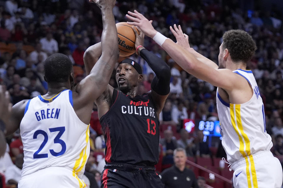 Miami Heat center Bam Adebayo (13) looks for an open teammate past Golden State Warriors forward Draymond Green (23) and guard Klay Thompson, right, during the first half of an NBA basketball game, Tuesday, March 26, 2024, in Miami. (AP Photo/Wilfredo Lee)