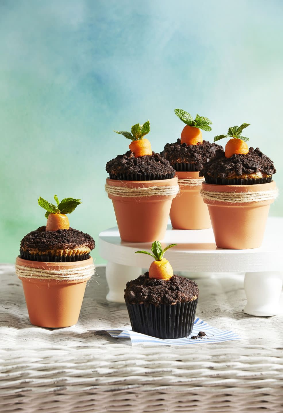 carrot patch cupcakes placed in mini terracotta pots and decorated to look like dirt on top with a carrot coming out