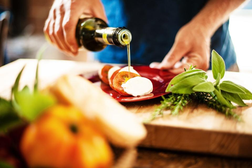 <p>Getty Images</p> Stock image of someone pouring olive oil on their Caprese salad