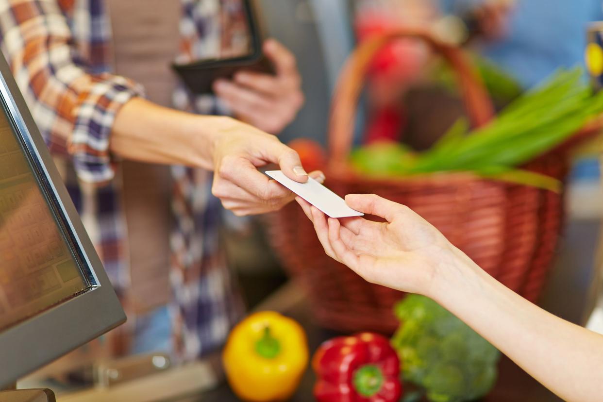 hand of customer giving credit card to supermarket cashier at checkout