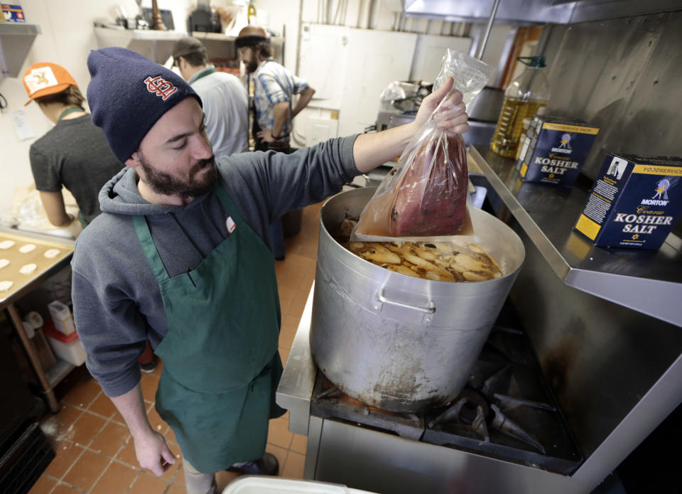 In this Dec. 11, 2013 photo, James Peisker places a vacuum-sealed bag containing a beef top round and a marinade in a pot to simmer for four hours as part of the process of preparing the "spiced round," a Christmastime beef specialty, at the Porter Road Butcher in Nashville, Tenn. The beef, which has already marinated for six days, will simmer for four hours. (AP Photo/Mark Humphrey)