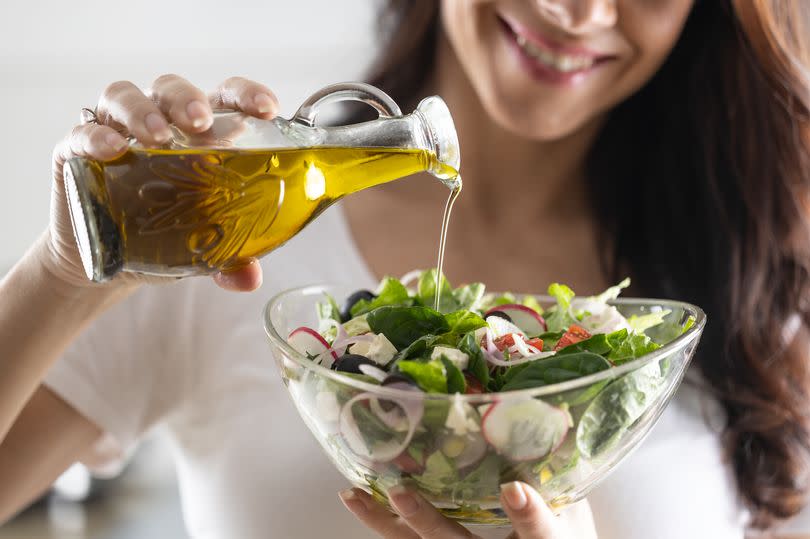 Young woman pouring olive oil into salad