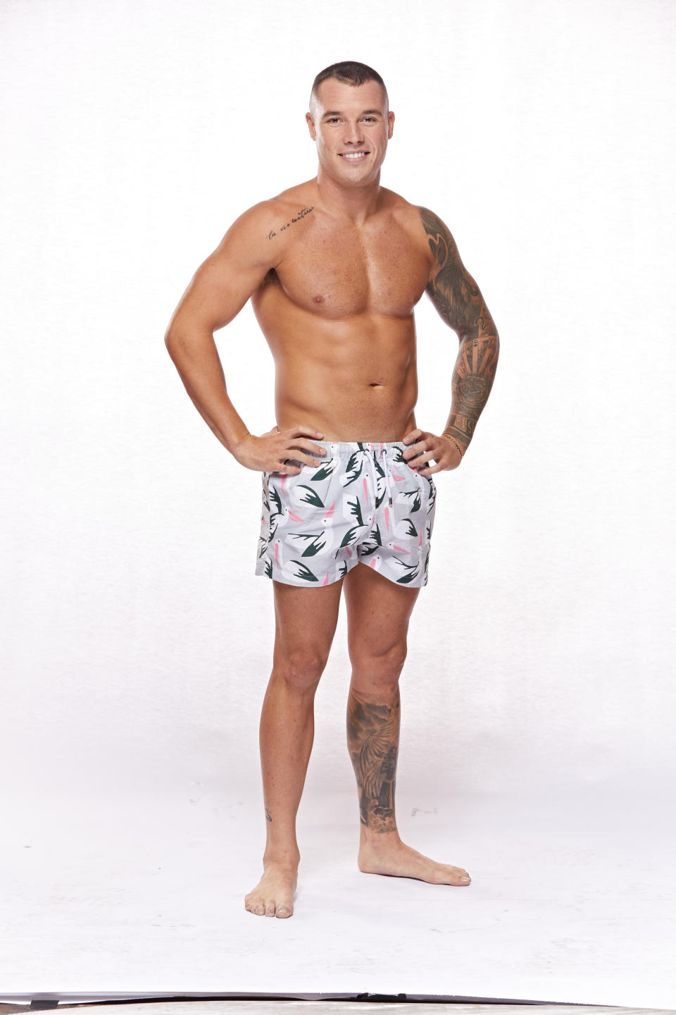 Contestant Connor stands smiling in board shorts against a white background