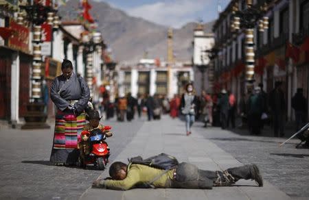 A child looks at a pilgrim kowtowing on a street outside Jokhang Monastery in Lhasa, Tibet autonomous region, March 6, 2014. REUTERS/Jacky Chen/File Photo