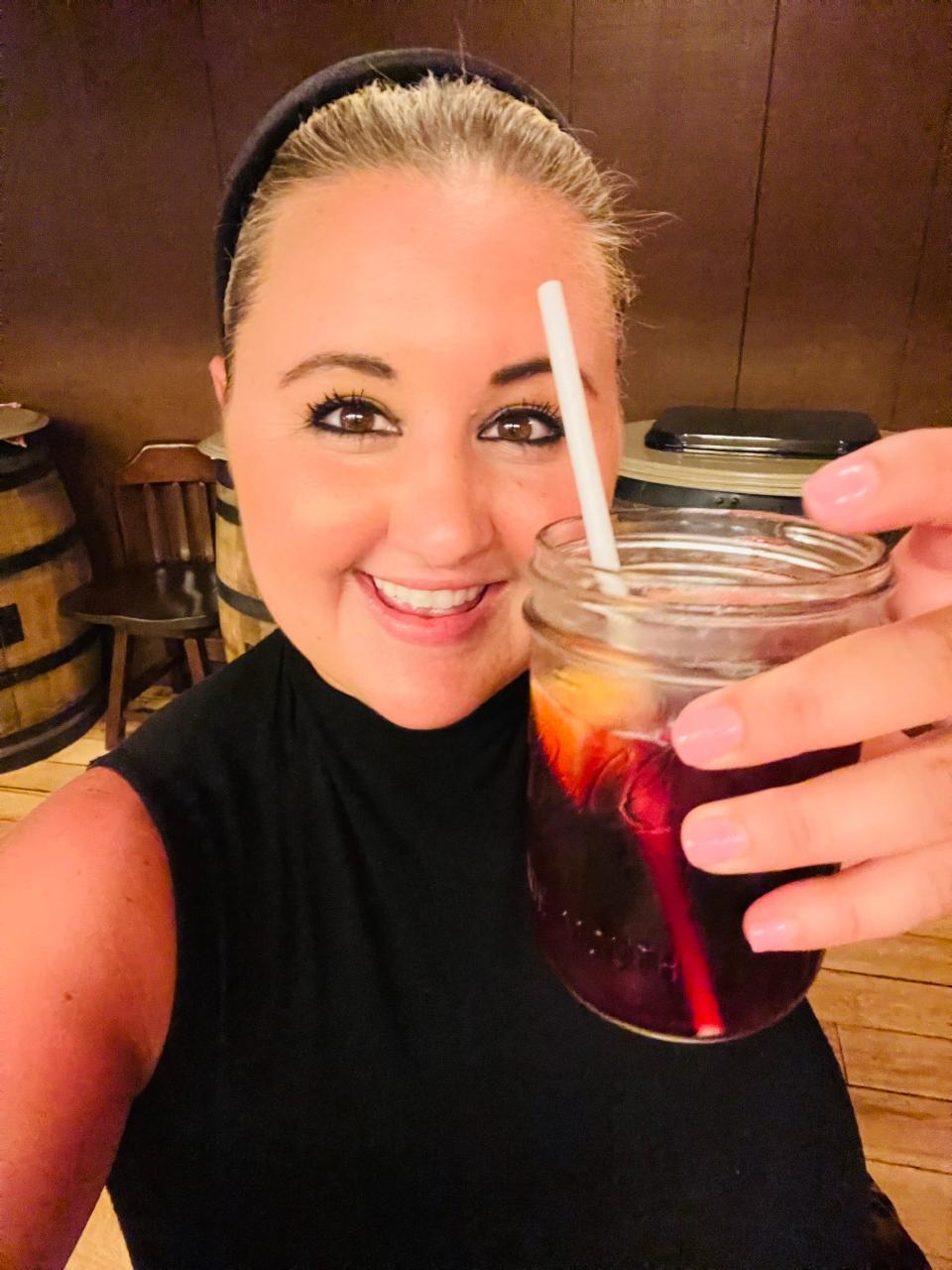 the writer holding a mason jar of sangria with a straw in it