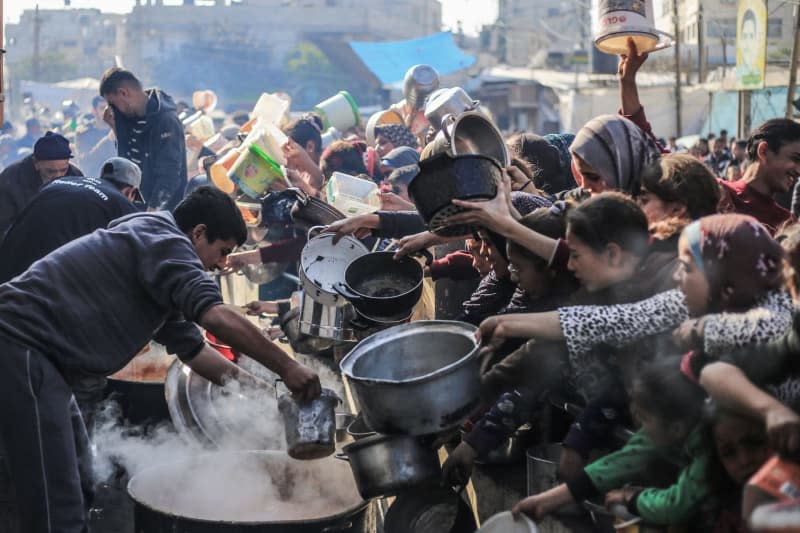 Palestinians receive food prepared in a charity kitchen amid a lack of food supplies as the fighting between Israel and Hamas continues. Mohammed Talatene/dpa