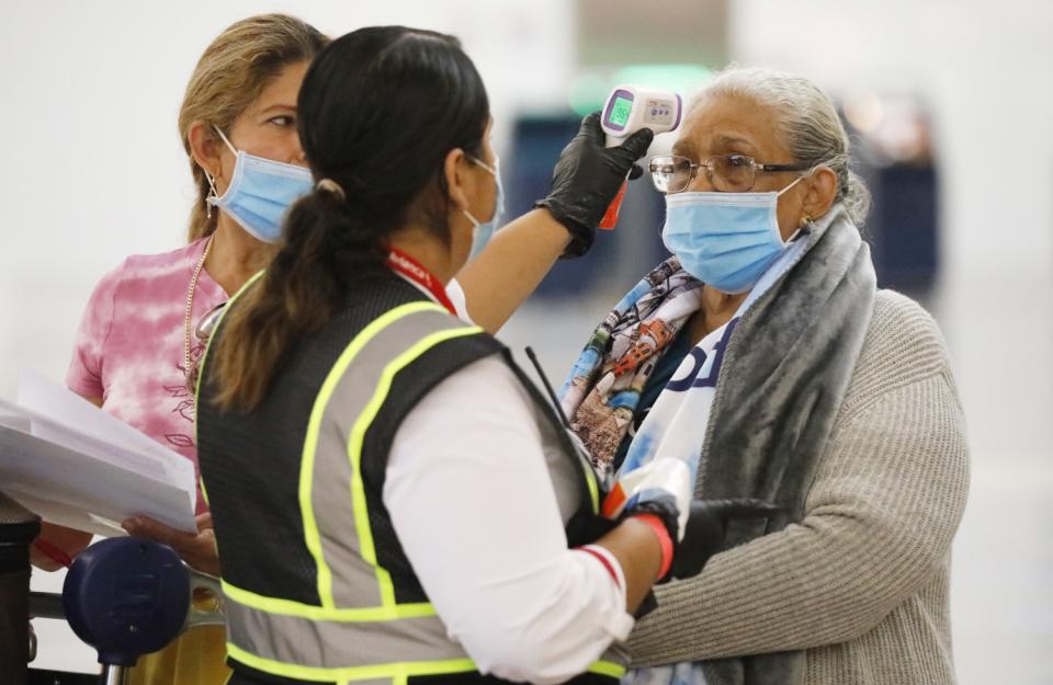 An Avianca employee at LAX takes a traveler's temperature.
