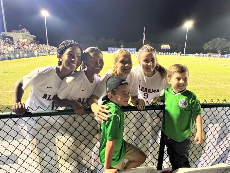 Alabama players take photo with two youth soccer boys following win in Tuesday's quarterfinal round of the SEC Women's Soccer Tournament at Ashton Brosnaham Soccer Complex