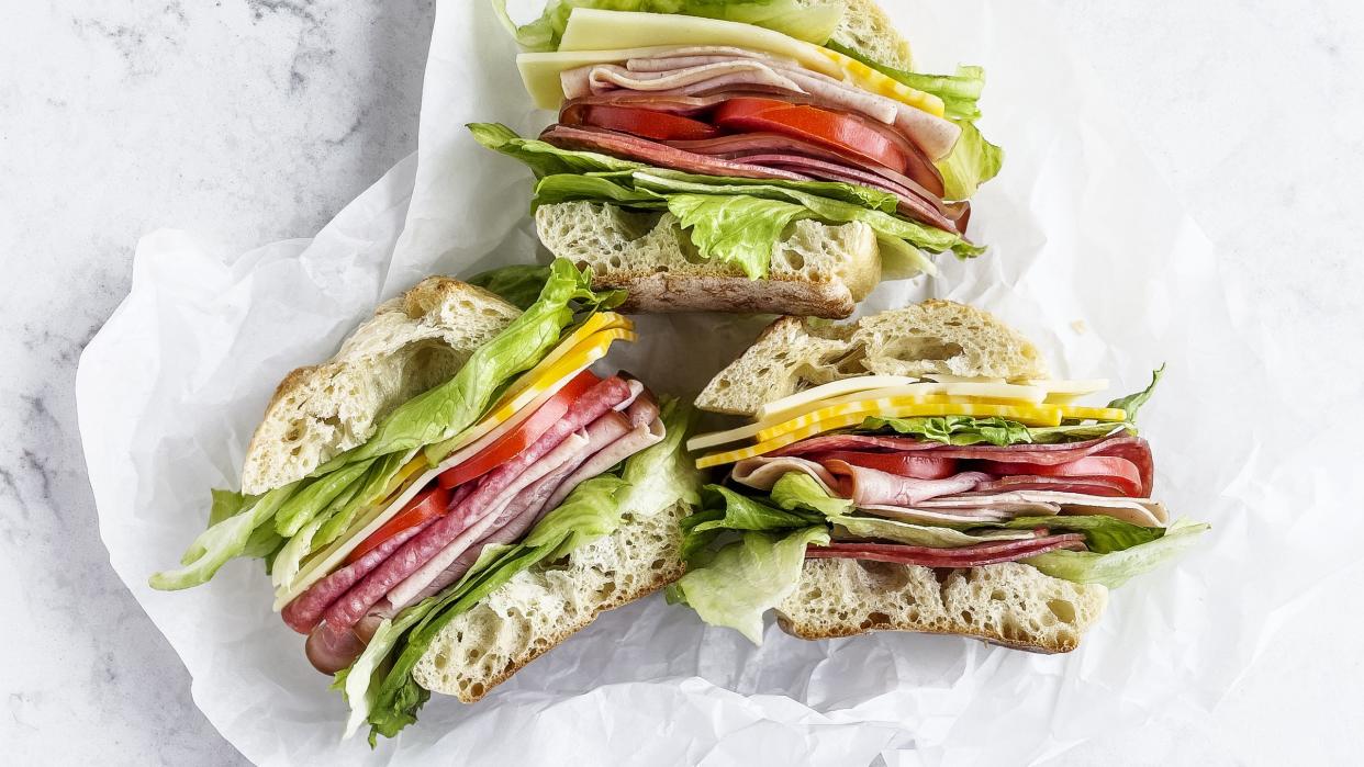 sandwiches with salami, ham, cheese, and tomatoes on parchment paper on white background