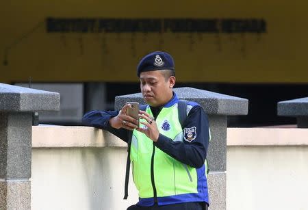 A police officer looks at his mobile phone as he stands guard outside the morgue at Kuala Lumpur General Hospital where Kim Jong Nam's body is held for autopsy in Malaysia, February 17, 2017. REUTERS/Athit Perawongmetha