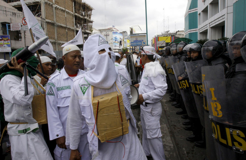 FILE - In this Nov. 23, 2012, file photo, a Muslim protester of Islam Defenders Front (FPI) wears a mock-suicide bomb during a demonstration against Israel's recent offensive against Palestinians in Gaza, outside the building that houses the U.S. consulate in Medan, North Sumatra, Indonesia. The Islamic Defenders Front, better known for vigilante actions against gays, Christmas decorations and prostitution, has over the past decade and a half repurposed its militia into a force that's as adept at searching for victims buried under earthquake rubble and distributing aid as it is at inspiring fear. (AP Photo/Binsar Bakkara, File)