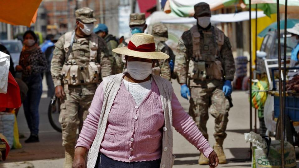 Mujer con mascarilla delante de dos soldados.