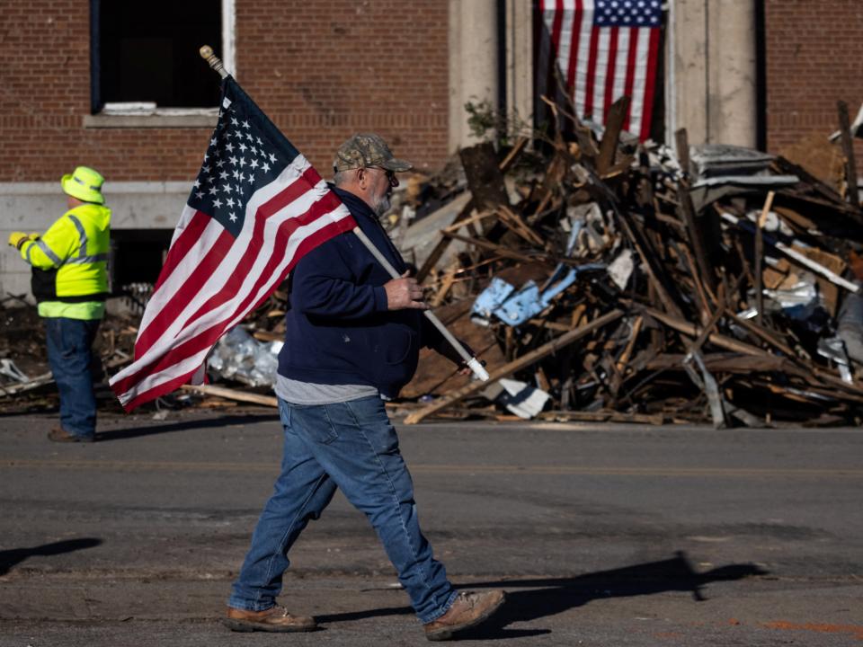 A local resident carries the U.S. flag past a pile of debris outside a post office in the aftermath of a tornado in Mayfield, Kentucky (REUTERS)