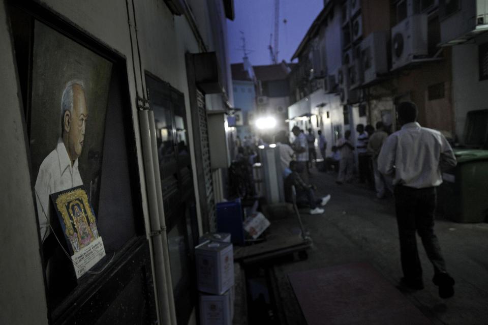 In this photo taken Feb. 9, 2014, a portrait of Singapore's first Prime Minister Lee Kuan Yew, left, is seen on a back alley where migrant workers congregate to enjoy their day off in Singapore's Little India District. Singapore’s wealth and continued growth rely in large part on foreign workers. Yet as the numbers of migrant workers soar, tales of abuse and exploitation are threatening to take some of the shine off the city-state’s international reputation. (AP Photo/Joseph Nair)