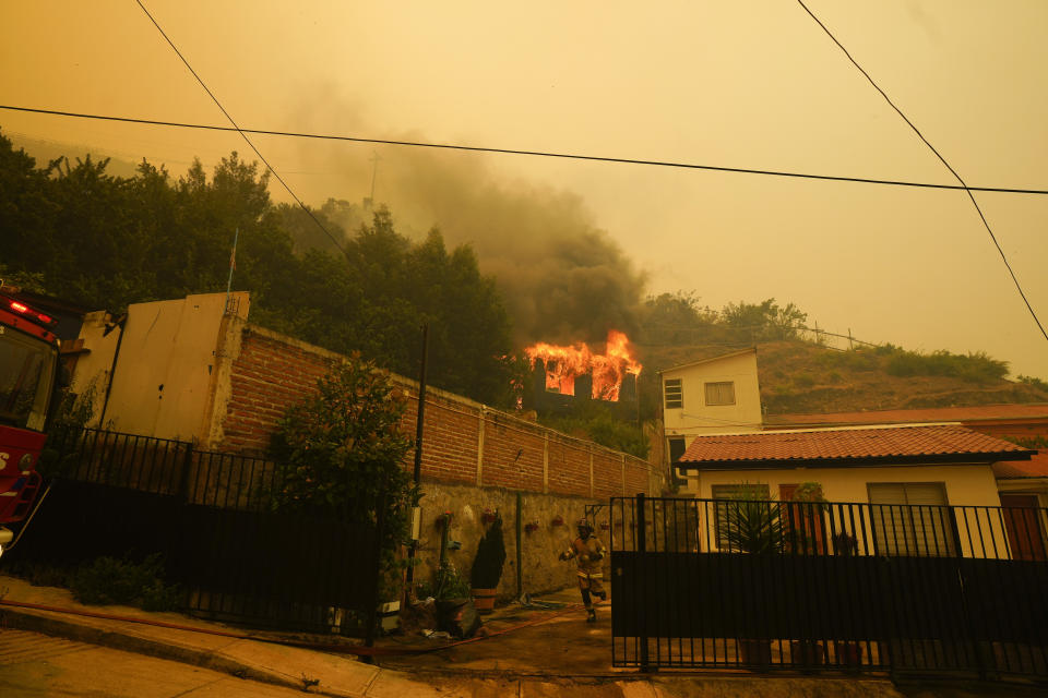 A firefighters runs through a front yard as a building goes up in flames, in Vina del Mar, Chile, Saturday, Feb. 3, 2024. Officials say intense forest fires burning around a densely populated area of central Chile have left several people dead and destroyed hundreds of homes. (AP Photo/Esteban Felix)