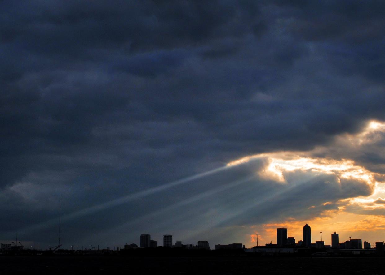 Sunlight streams through a blanket of heavy clouds over the downtown Jacksonville skyline.