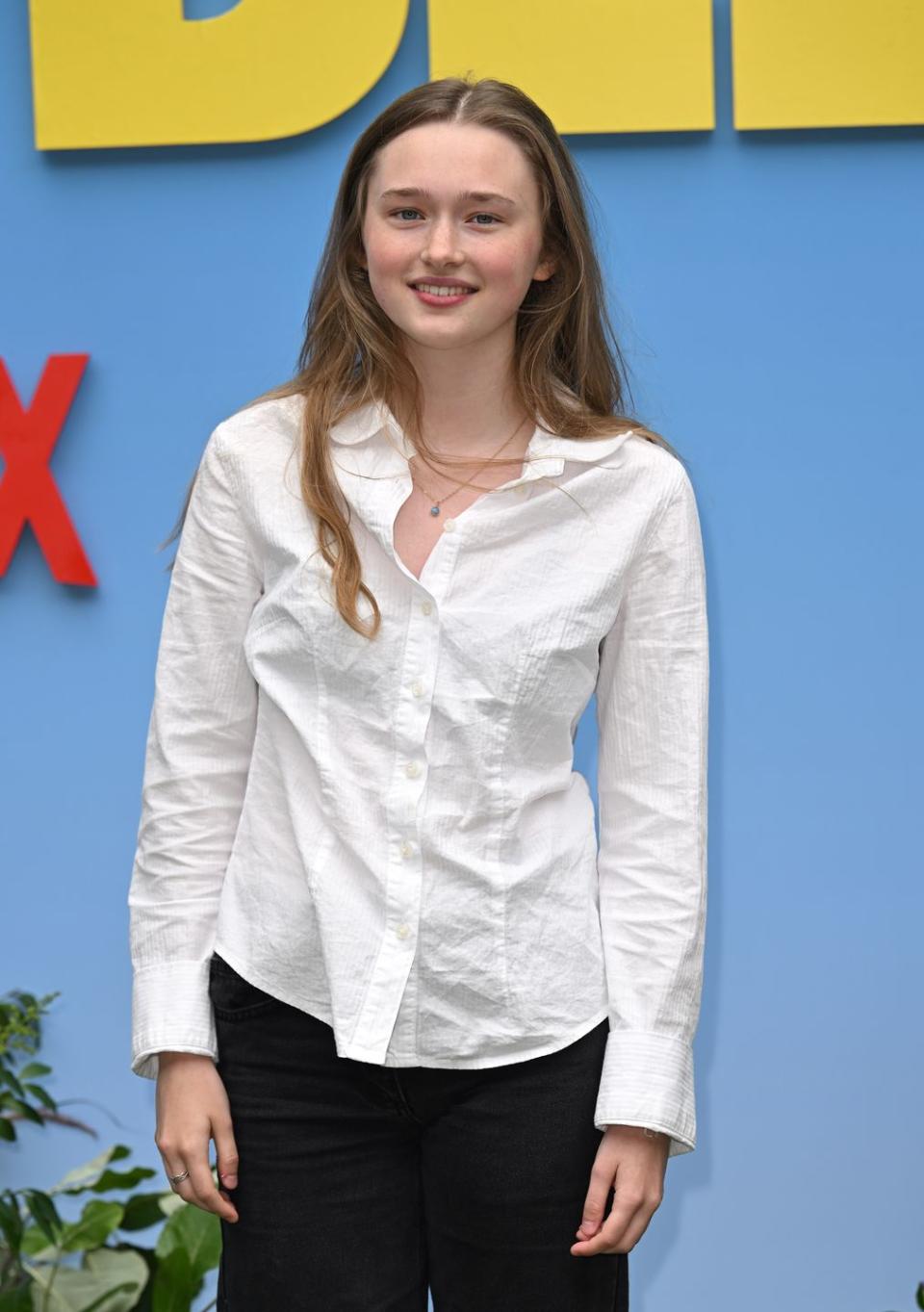 india fowler, a young woman stands smiling, she wears a white blouse with black trousers and has long light brown hair worn loose