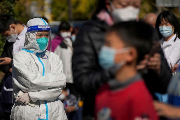 PHOTO: A worker in protective suit stands watch as masked residents wait in line to get their routine COVID-19 throat swabs tests at a coronavirus testing site in Beijing, Oct. 18, 2022. (Andy Wong/AP)