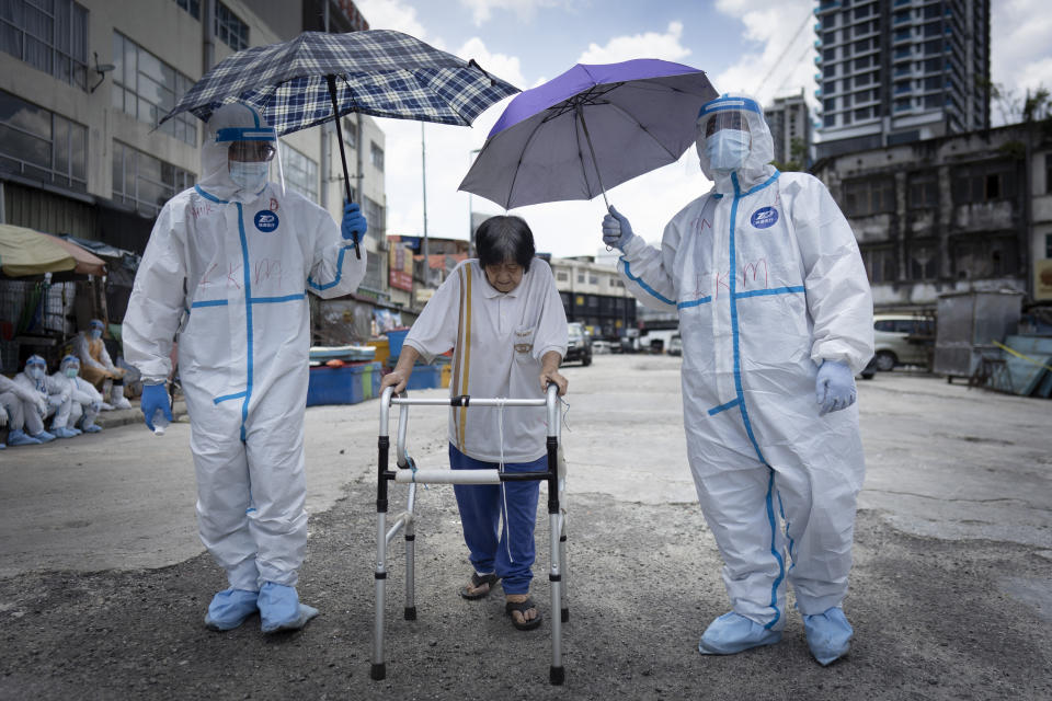 Health officials escort an elderly women back home under hot sun after she had a coronavirus test at a wet market in Kuala Lumpur, Malaysia, on Tuesday, May 5, 2020. Malaysia's government says all foreign workers must undergo mandatory virus testing as many business sectors reopen in parts of the country for the first time since a partial virus lockdown began March 18. (AP Photo/Vincent Thian)