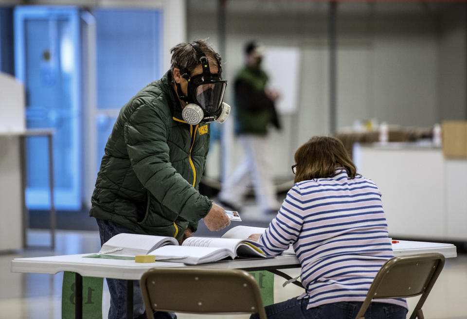 Robert Forrestal, left, wears a full face chemical shield to protect against the spread of coronavirus, as he votes Tuesday, April 7, 2020, at the Janesville Mall in Janesville, Wis. Hundreds of voters in Wisconsin are waiting in line to cast ballots at polling places for the state's presidential primary election, ignoring a stay-at-home order over the coronavirus threat. (Angela Major/The Janesville Gazette via AP)